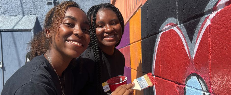 Two students pose outside painting at a local service opportunity.